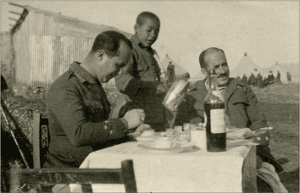 Dos oficiales españoles se disponen a comer, servidos por un niño moro en el zoco el Arbaa de Beni Hassan en 1926. Álbum del coronel Rafael Tejero Saurina. Museo del Ejército