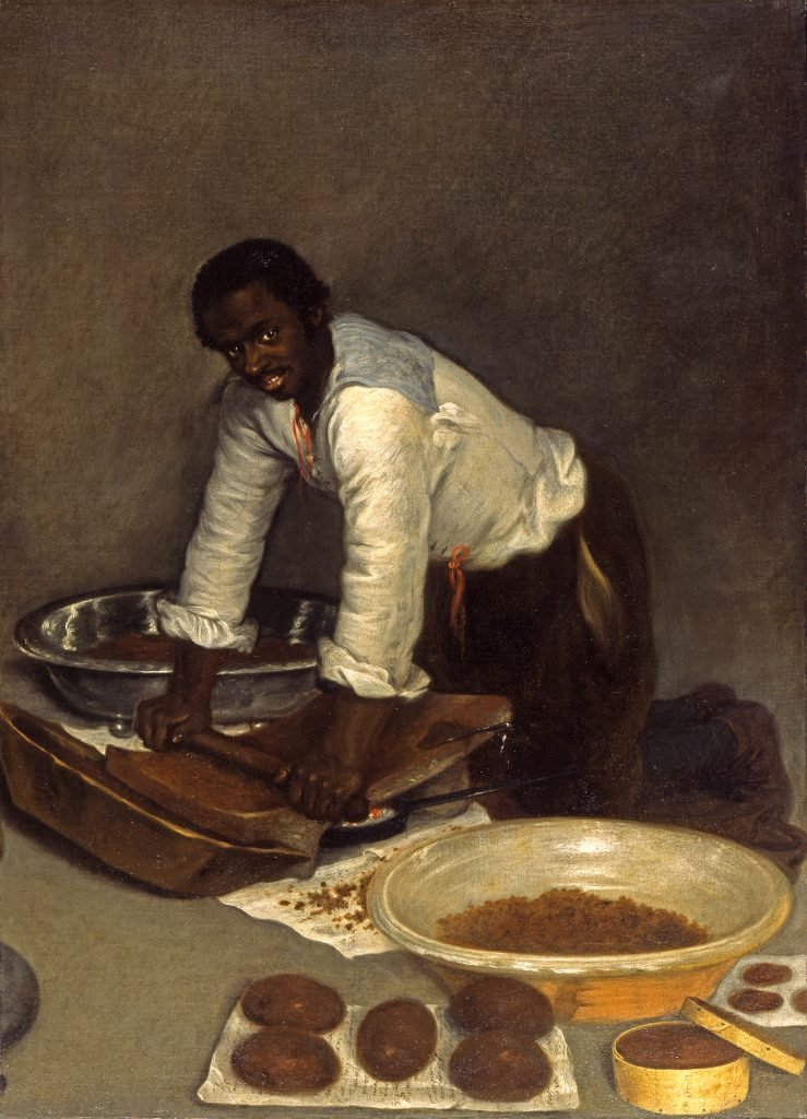 Un hombre negro moliendo cacao para hacer chocolate con un metate (siglo XVIII)